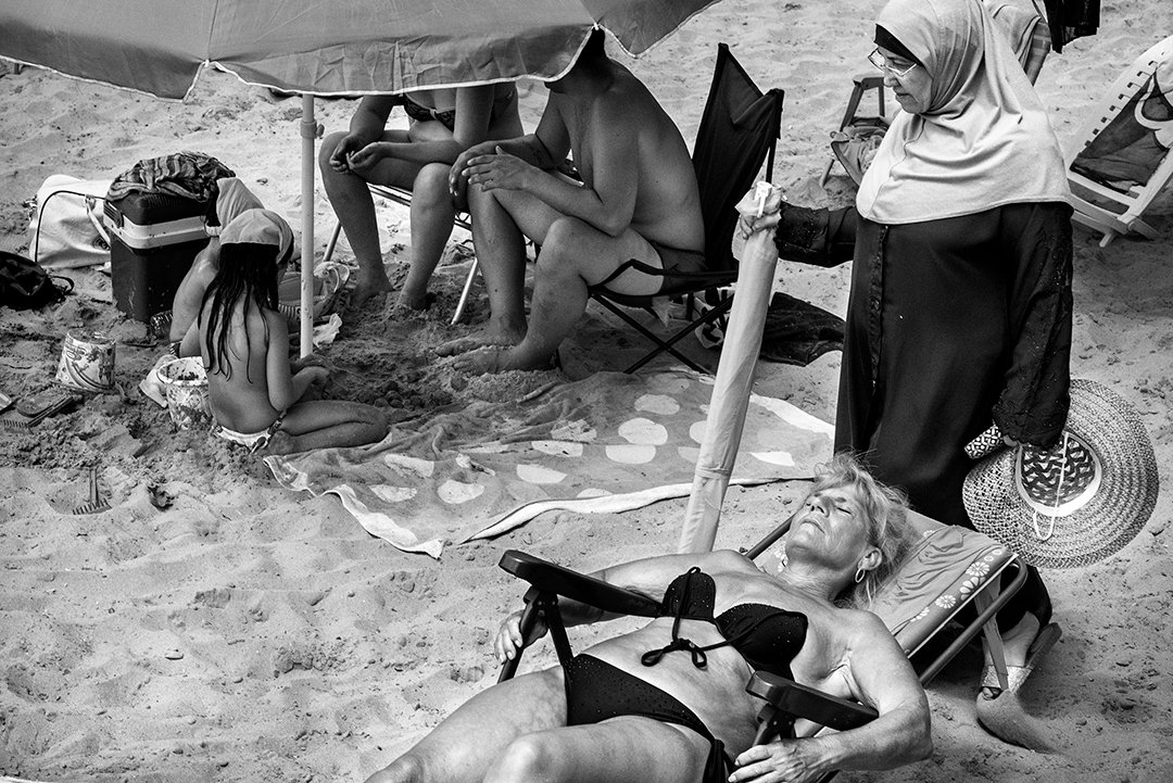 People rest beneath umbrellas and on the sand.